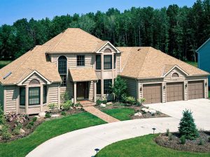 Luxury home with tan roof and siding, brown garage doors, and bay windows